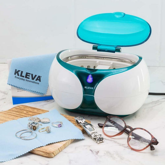 A jewellery cleaner surrounded by reading glasses, jewellery, a watch and a blue cloth.
