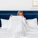 A woman sitting behind luxurious bed linens on a lavish bed.