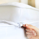 A manicured hand zips a white Super Sleeper Pro Replacement Cover for the Wave Topper, featuring a mesh panel and zipper, over a mattress.