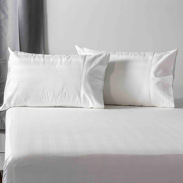 A large, soft bed featuring two white pillows which are complimented with sleek, cotton pillowcases.