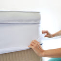 A person fits the Super Sleeper Pro Replacement Cover for Wave Topper over a mattress corner, both hands holding the bamboo viscose fabric. The white mattress rests on a beige box spring, highlighting this premium cover by Super Sleeper Pro.